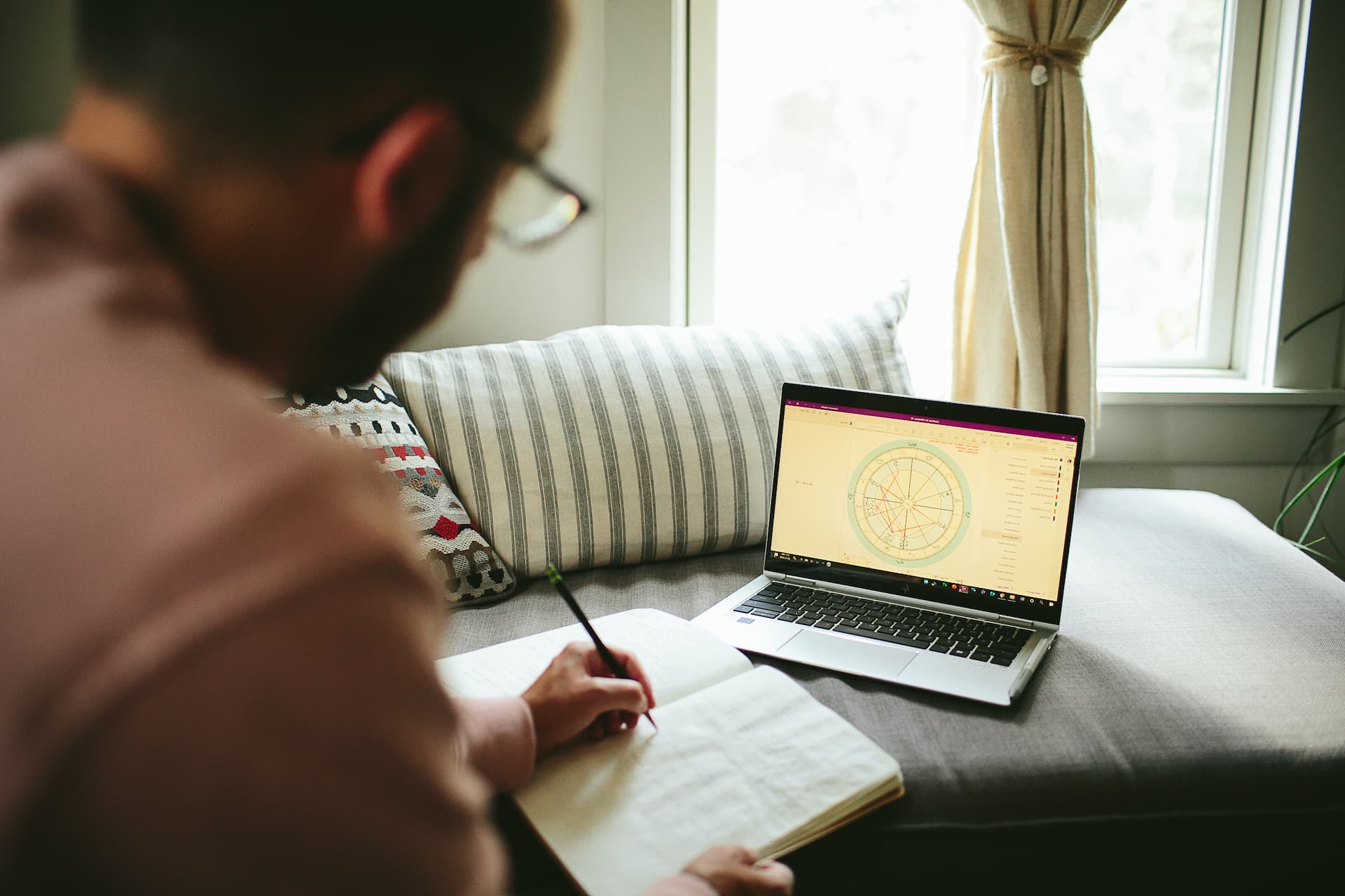 Reviewing a birth chart on a laptop while journaling by a sunlit window